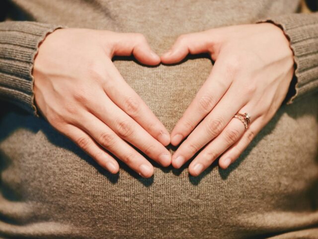 hands making a heart shape atop of a pregnant tummy
