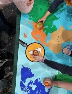 children's hands placing fruit on a large map on a table