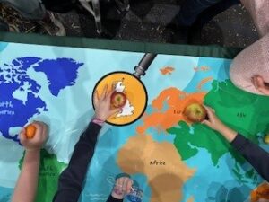 children's hands placing fruit on a large map on a table