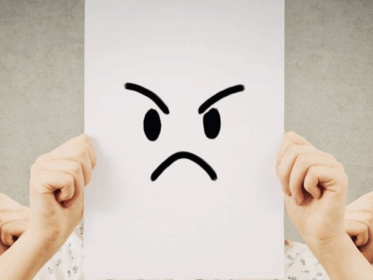 grumpy face drawn on to piece of paper, held up in front of a persons head